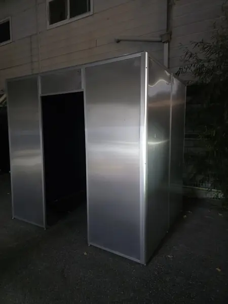야간 골목에 설치된 은색 알루미늄 박스형 부스 — 반쯤 열린 출입구