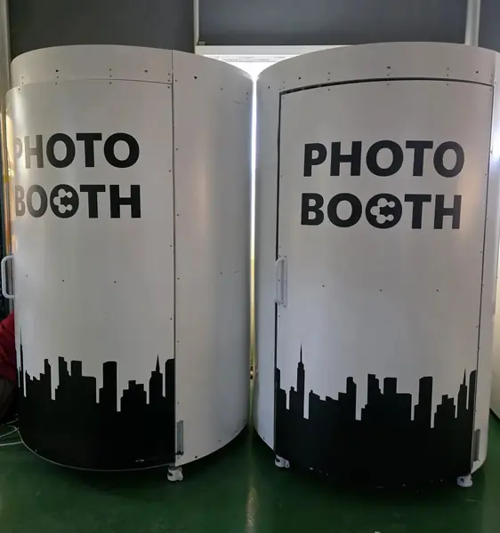 흰색 원통형 하이앵글부스 2대 — 'PHOTO BOOTH' 글자와 하단 도시 실루엣 그래픽