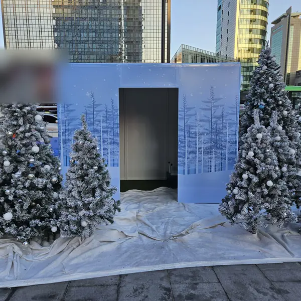 도심 광장 크리스마스 행사장의 겨울숲 4면 랩핑 스탠다드 부스 — 눈 덮인 트리 장식 사이 출입구