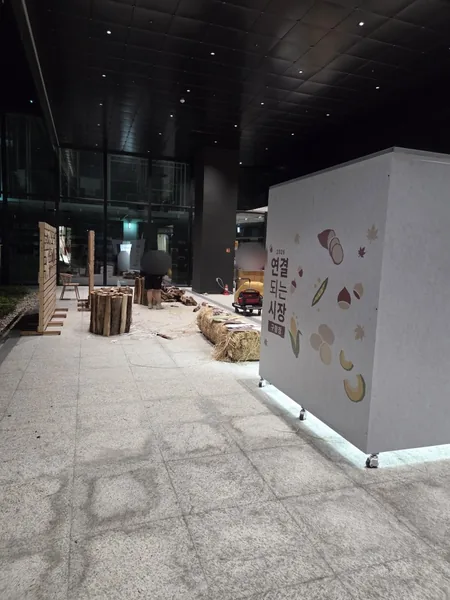 무인양품 랩핑 부스 옆면 — 바닥에서 올라오는 간접조명, 뒤쪽은 행사 준비 중인 광장