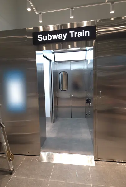 'Subway Train' 간판을 단 지하철부스 정면 — 스테인리스 객차 문과 둥근 창, 손잡이 봉이 보이는 출입구